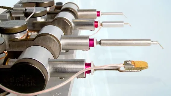 Four MM3A-EM manipulators in a row, each fitted with a different probe tip; the nearest holds a gold-coloured sample chip.