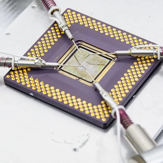 Top-down view of four tungsten probe tips landed on the exposed die of a ceramic pin-grid-array package.