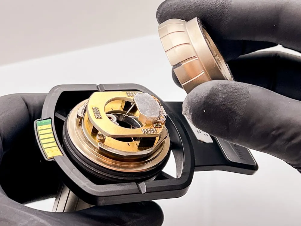 A gloved hand lifting a gold-plated plug-in tool out of the black Phenom sample-holder frame, mid tool exchange.
